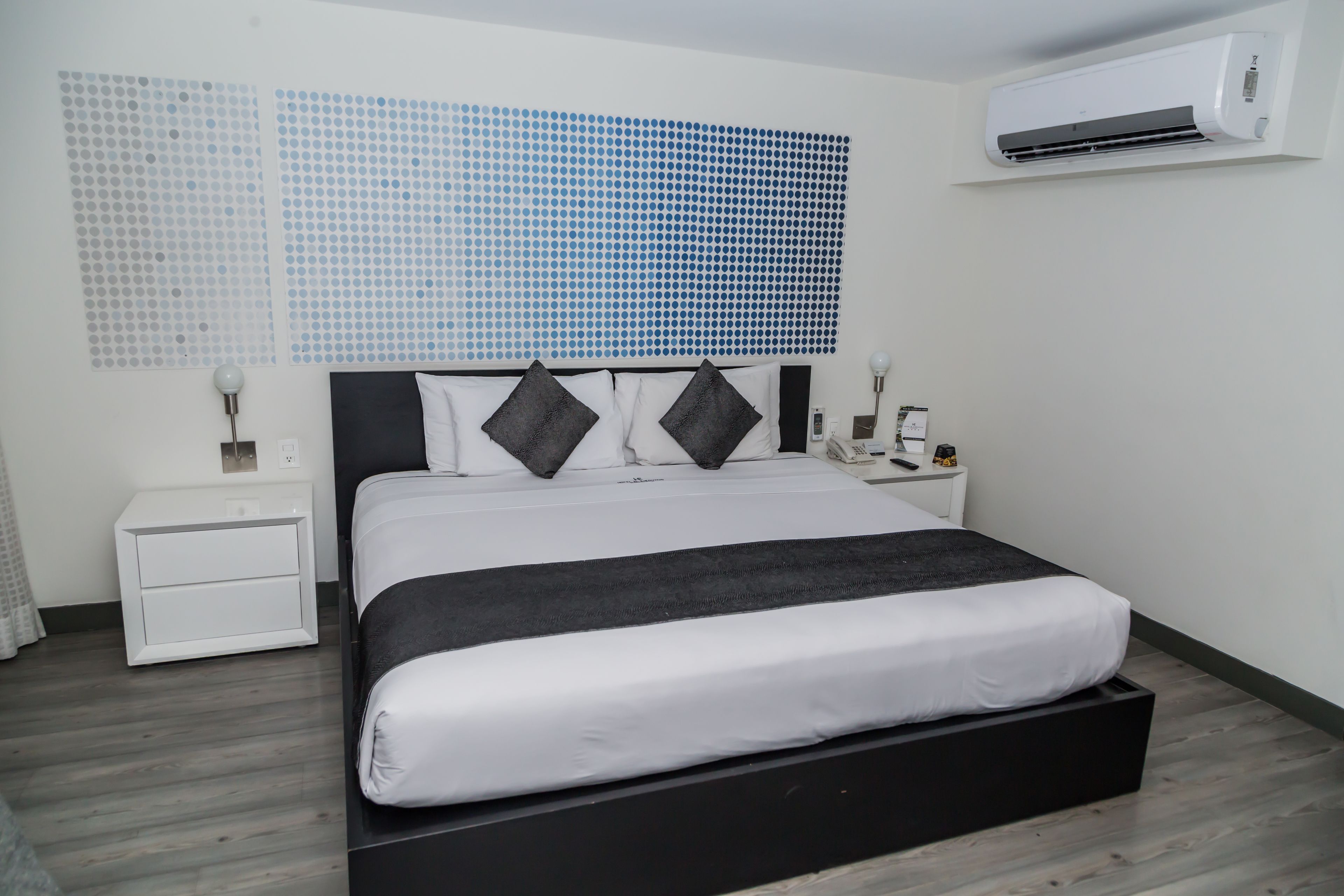 Ein modernes Schlafzimmer mit einem großen Bett, weißen Nachttischen und einer an der Wand montierten Klimaanlage.
