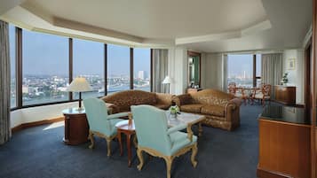 A hotel room with a large window, a sofa set, a dining table with chairs, and a small desk.