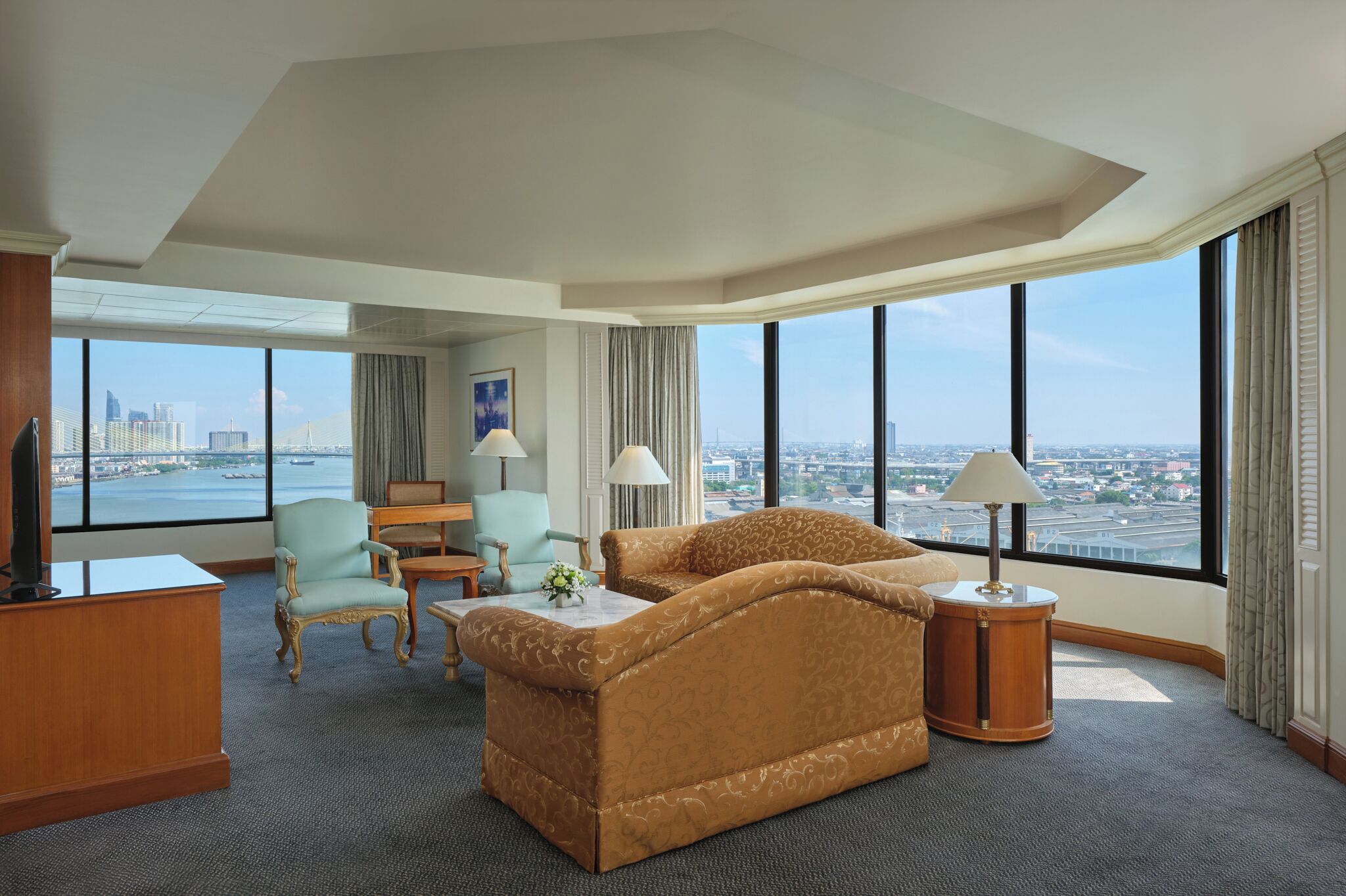 A hotel room with a large window, a sofa, a desk, a chair, and a lamp.