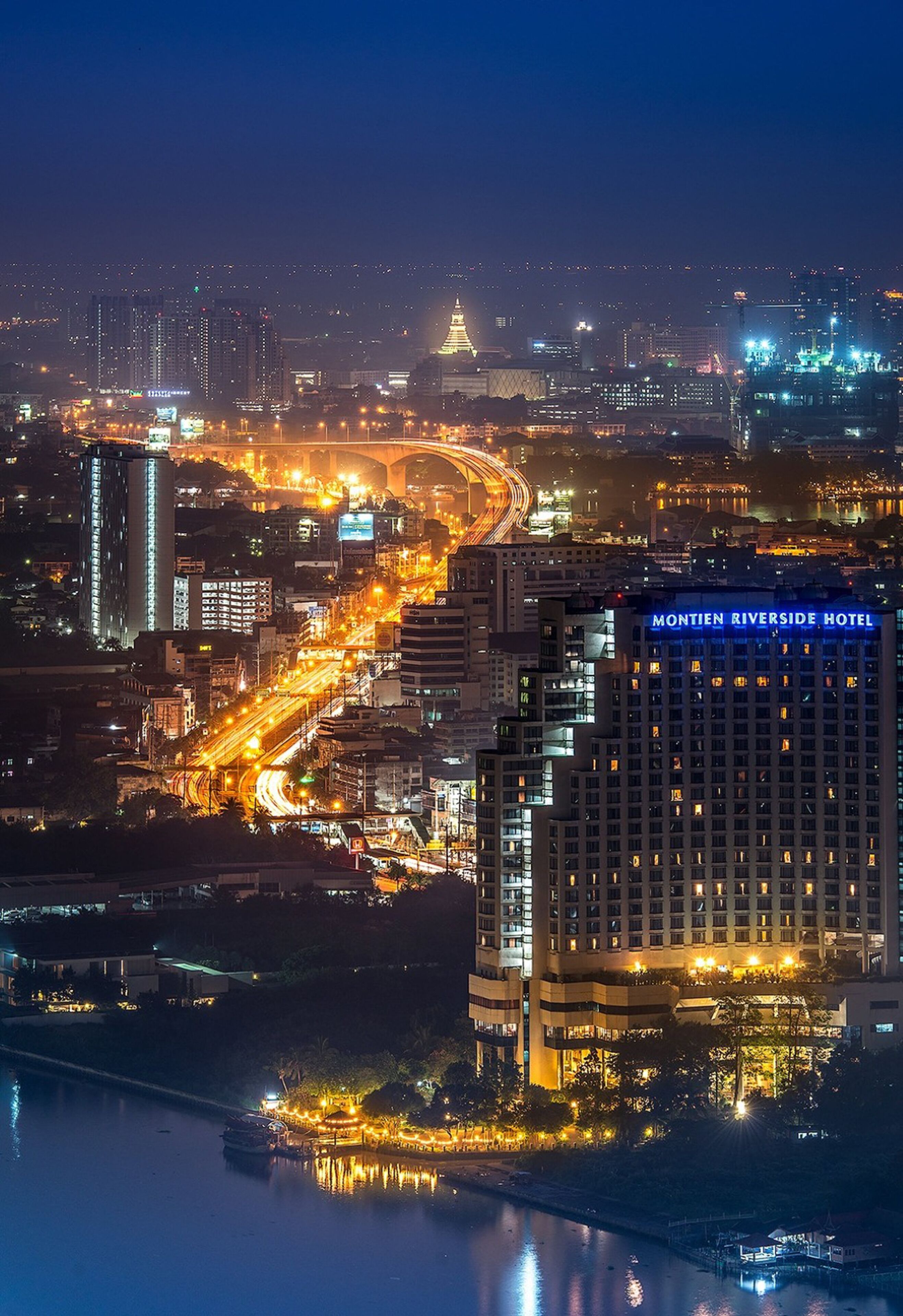 A nighttime cityscape with the Montien Riverside Hotel prominently lit.