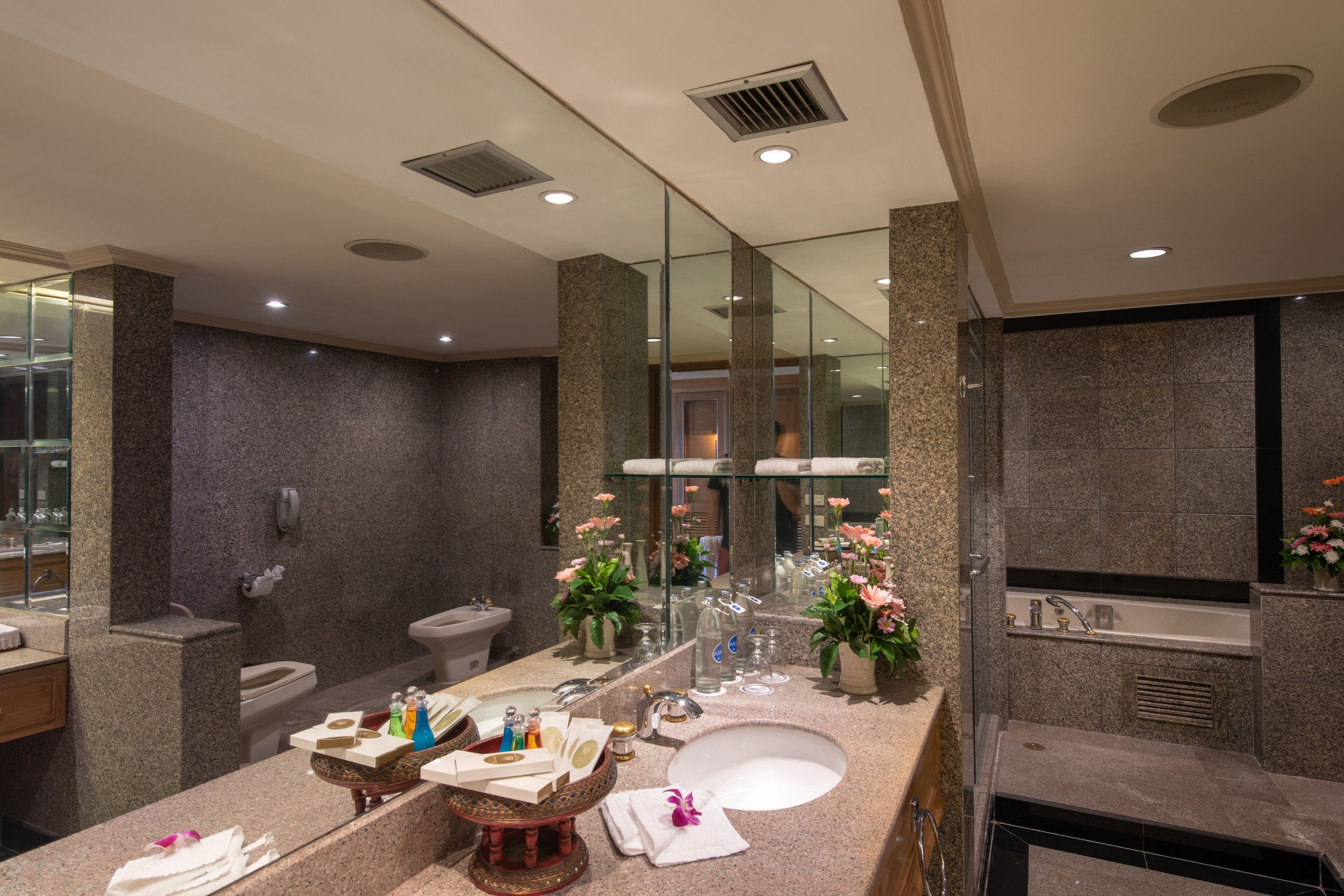 A modern bathroom with a large mirror, granite countertops, a sink, and a bathtub.