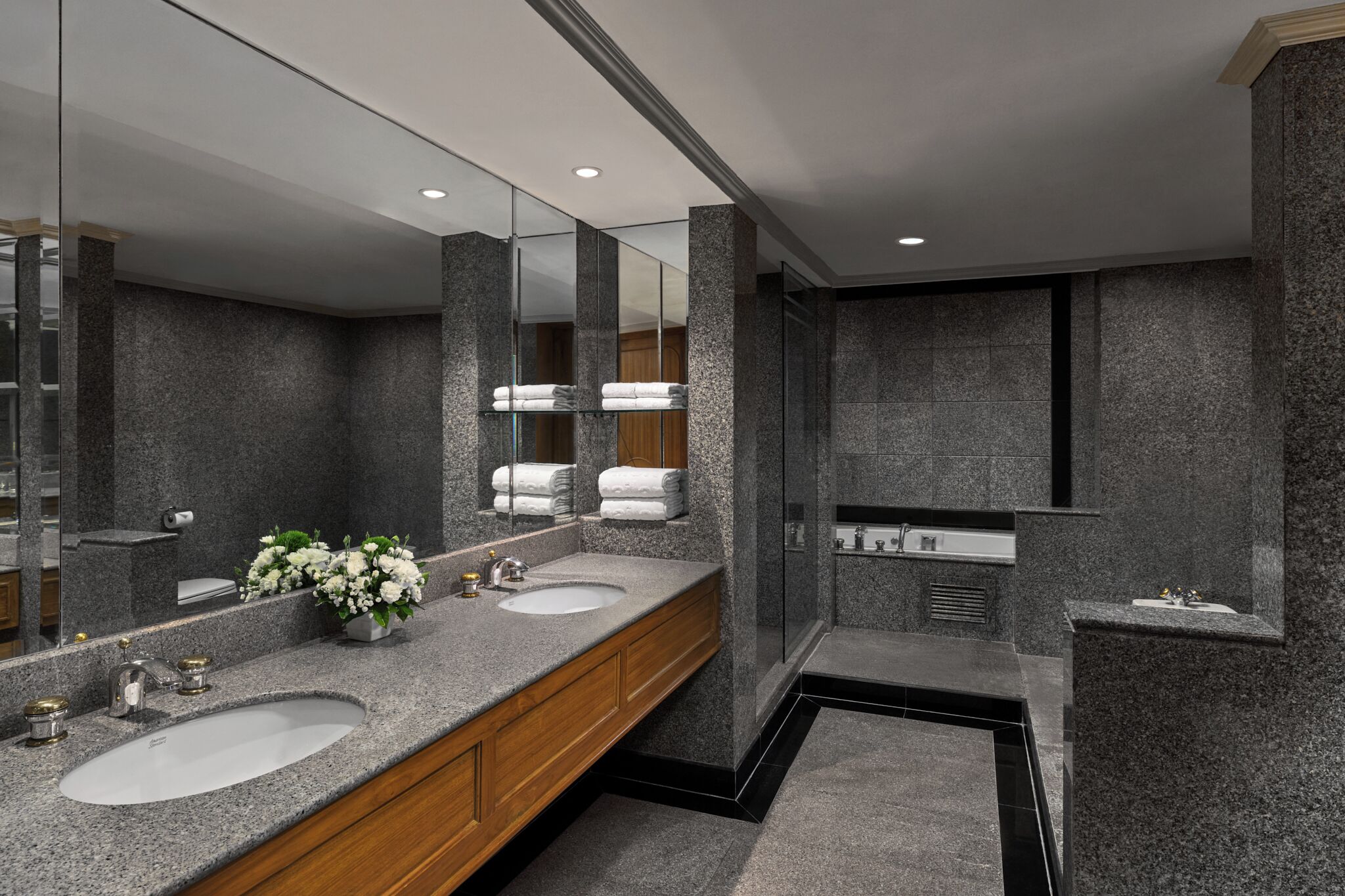 A modern bathroom with granite countertops, two sinks, a large mirror, and a shower area.