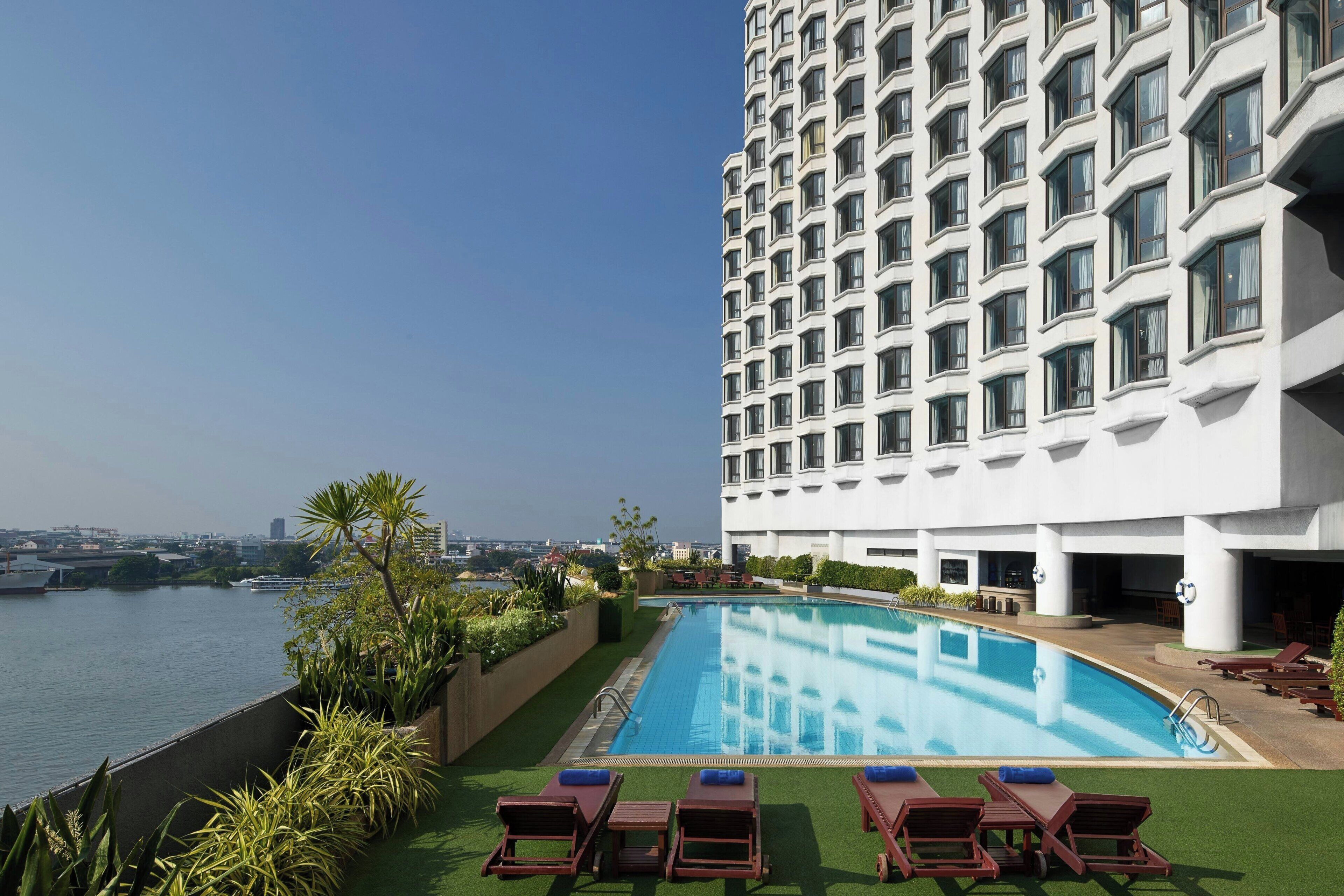 A hotel with a swimming pool, lounge chairs, and a view of the water.