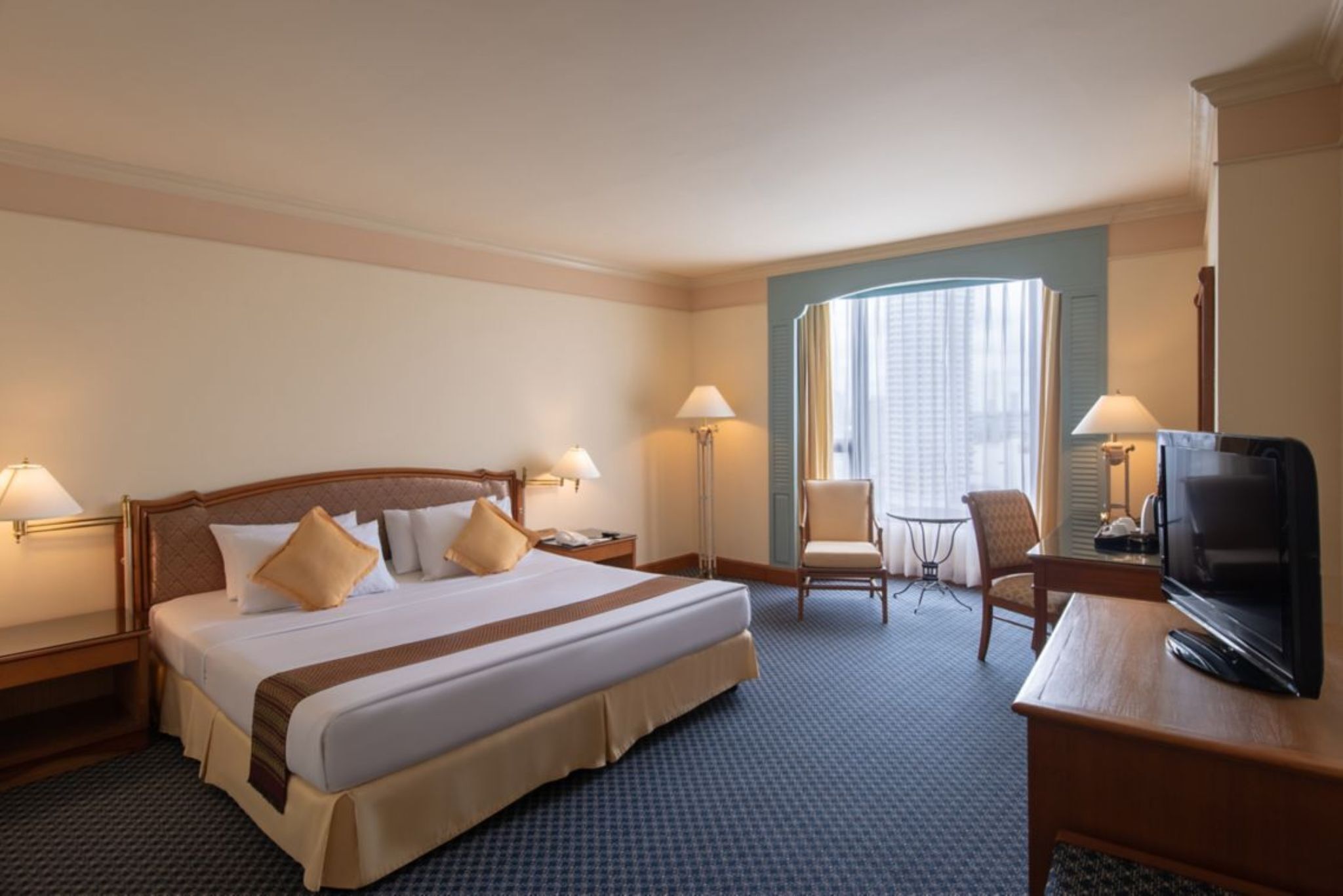 A hotel room with a large bed, two bedside tables, a TV, a chair, and a small table.