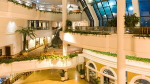 Ein mehrgeschossiges Atrium mit einem zentralen, kreisförmigen Design im Boden, mehreren Etagen mit Balkonen und großen Fenstern, die natürliches Licht hereinlassen.