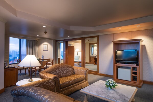 Habitación de hotel con sofá, mesa de centro, televisión y vistas a la ciudad.