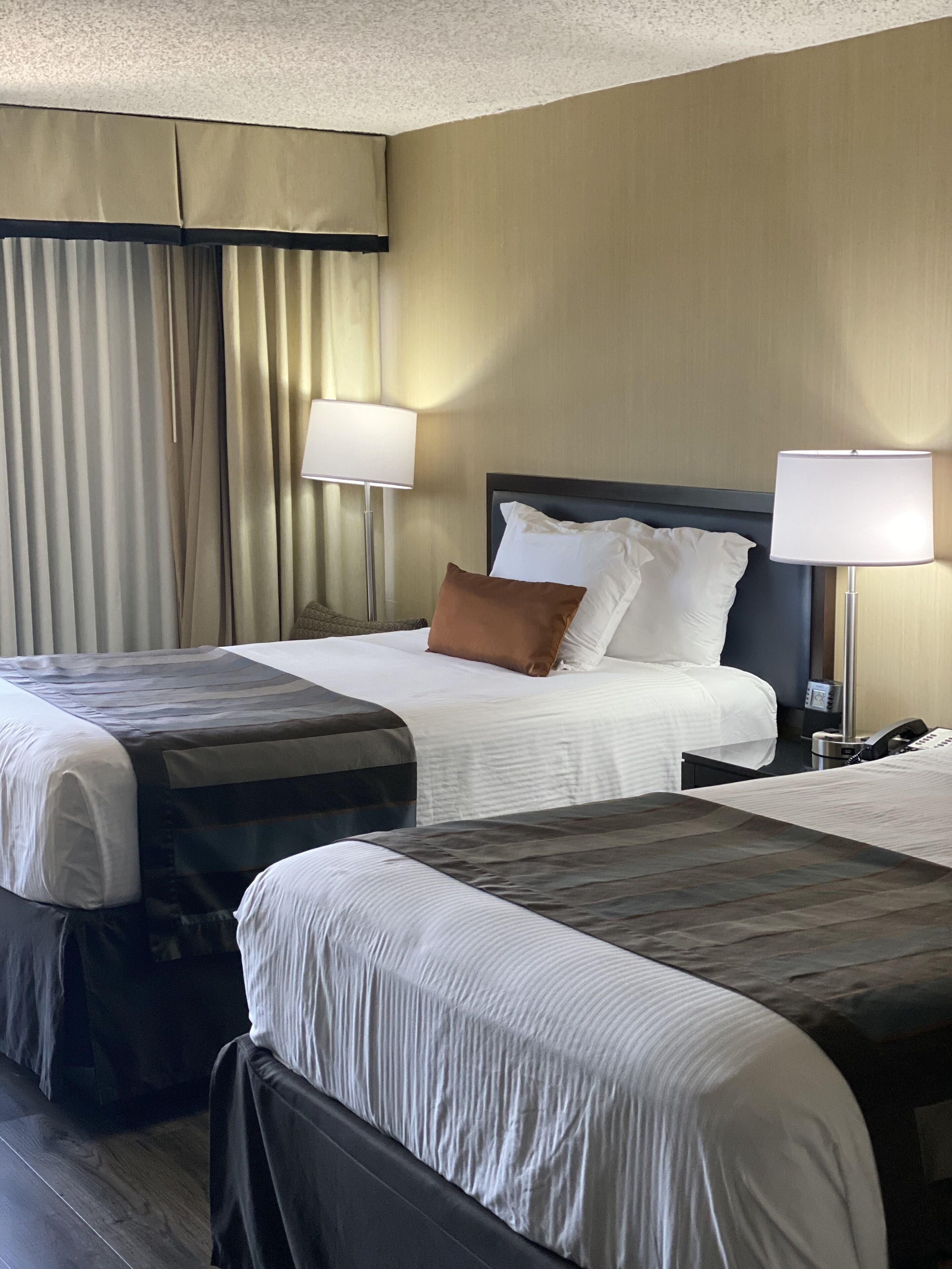 A hotel room with two beds, a large window with curtains, and two bedside lamps.