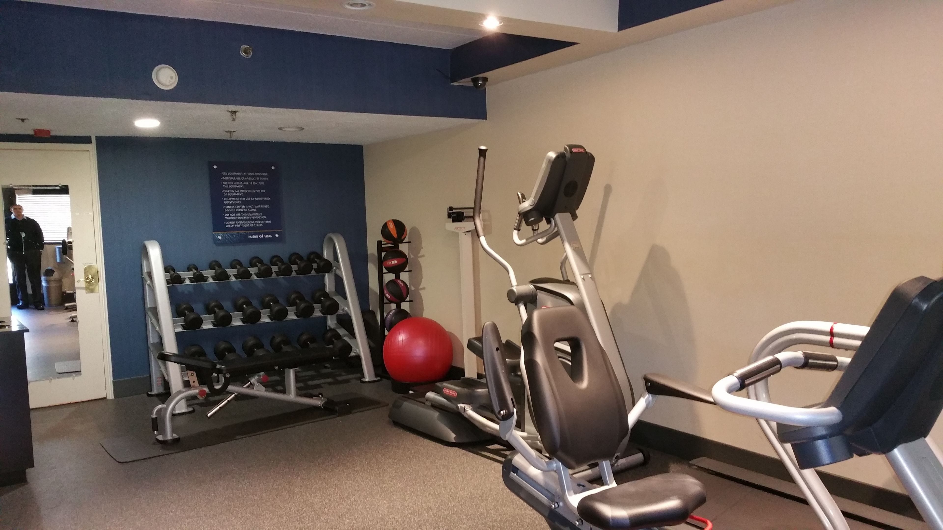 Un gimnasio con equipo de ejercicio, un estante con mancuernas y una pelota de ejercicios roja.