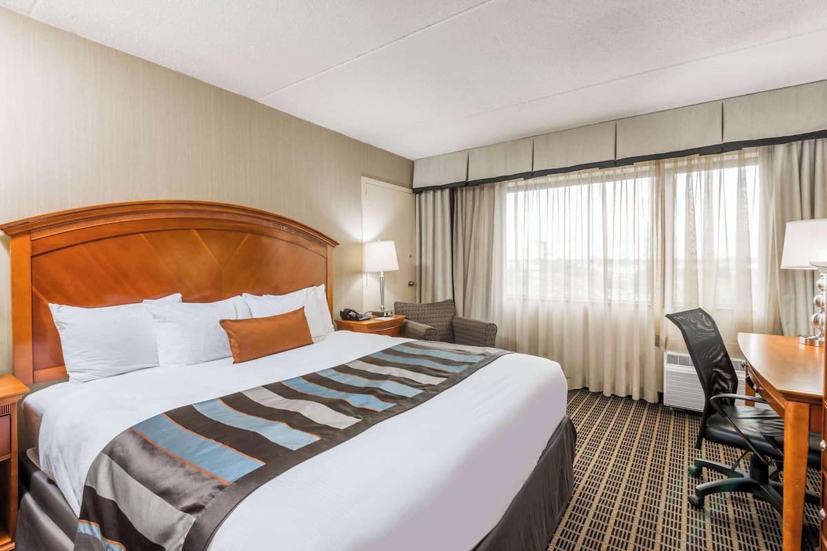 A hotel room with a large bed, a desk, a chair, a lamp, and a window with curtains.