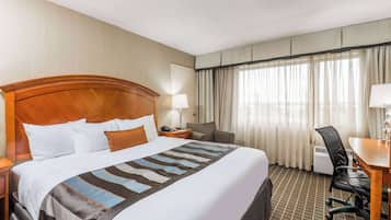 A hotel room with a large bed, a desk, a chair, a lamp, and a window with curtains.
