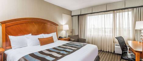 A hotel room with a large bed, a desk, a chair, a lamp, and a window with curtains.