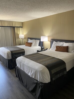 A hotel room with two beds, each with a pillow and a bedside lamp.