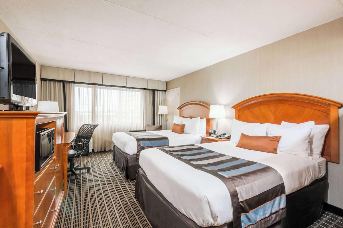 A hotel room with two beds, a desk with a television, and a chair.