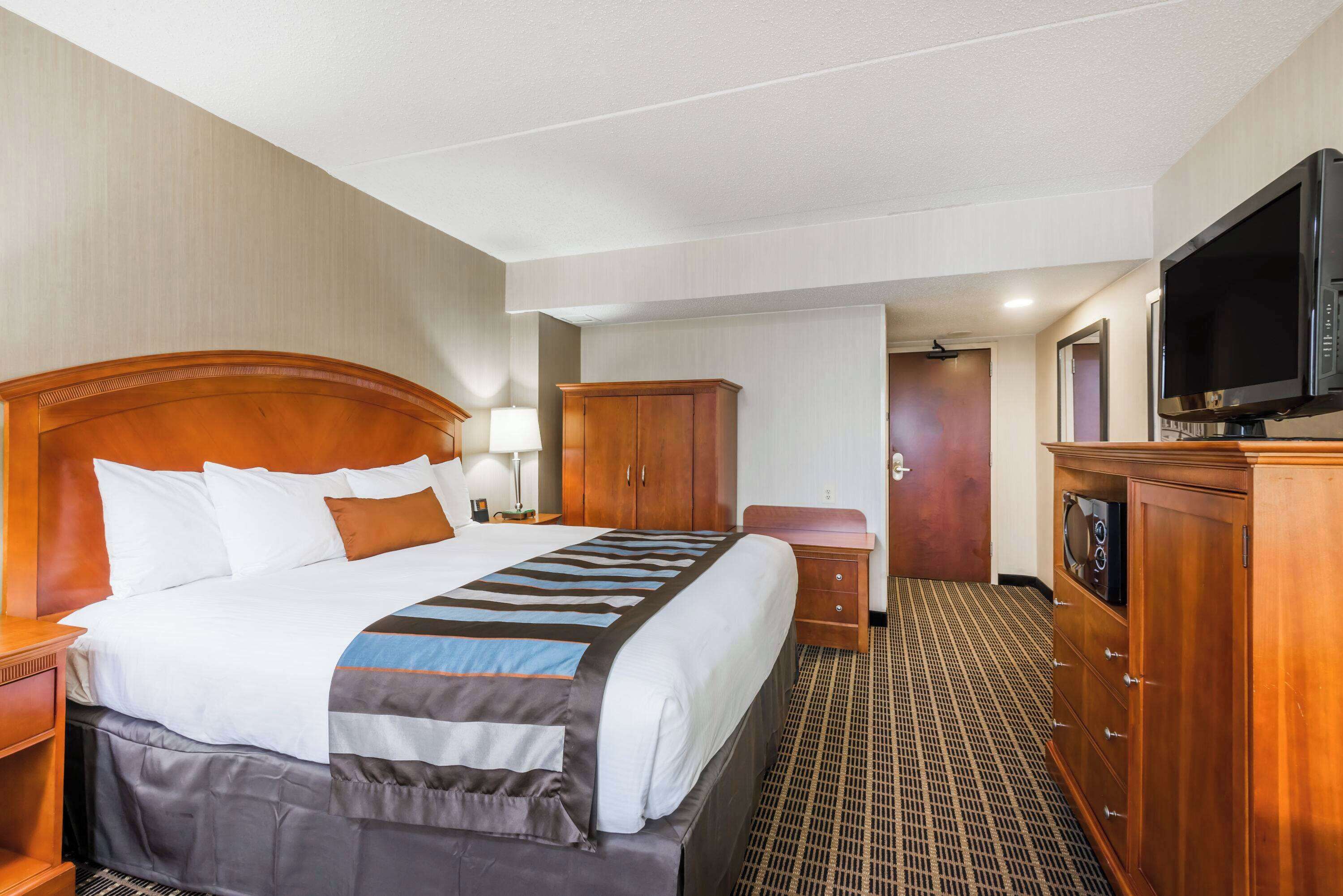Habitación de hotel con una cama grande, cabecera de madera, un aparador, televisor y piso alfombrado.