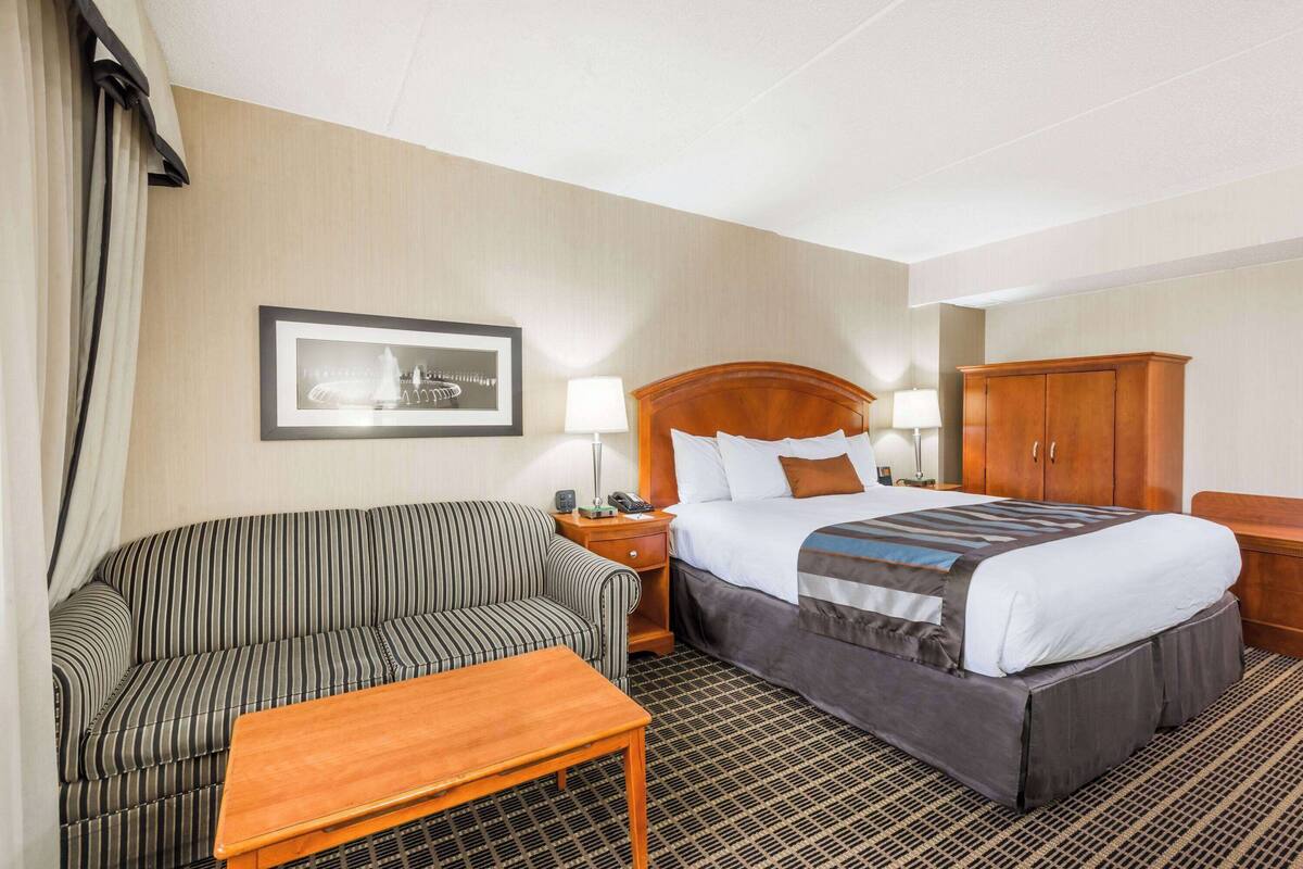 A hotel room with a bed, a sofa, a nightstand, and a wooden cabinet.
