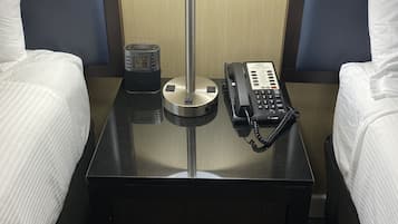 Een hotelkamer met twee bedden, een nachtkastje met een lamp, een klok en een telefoon.