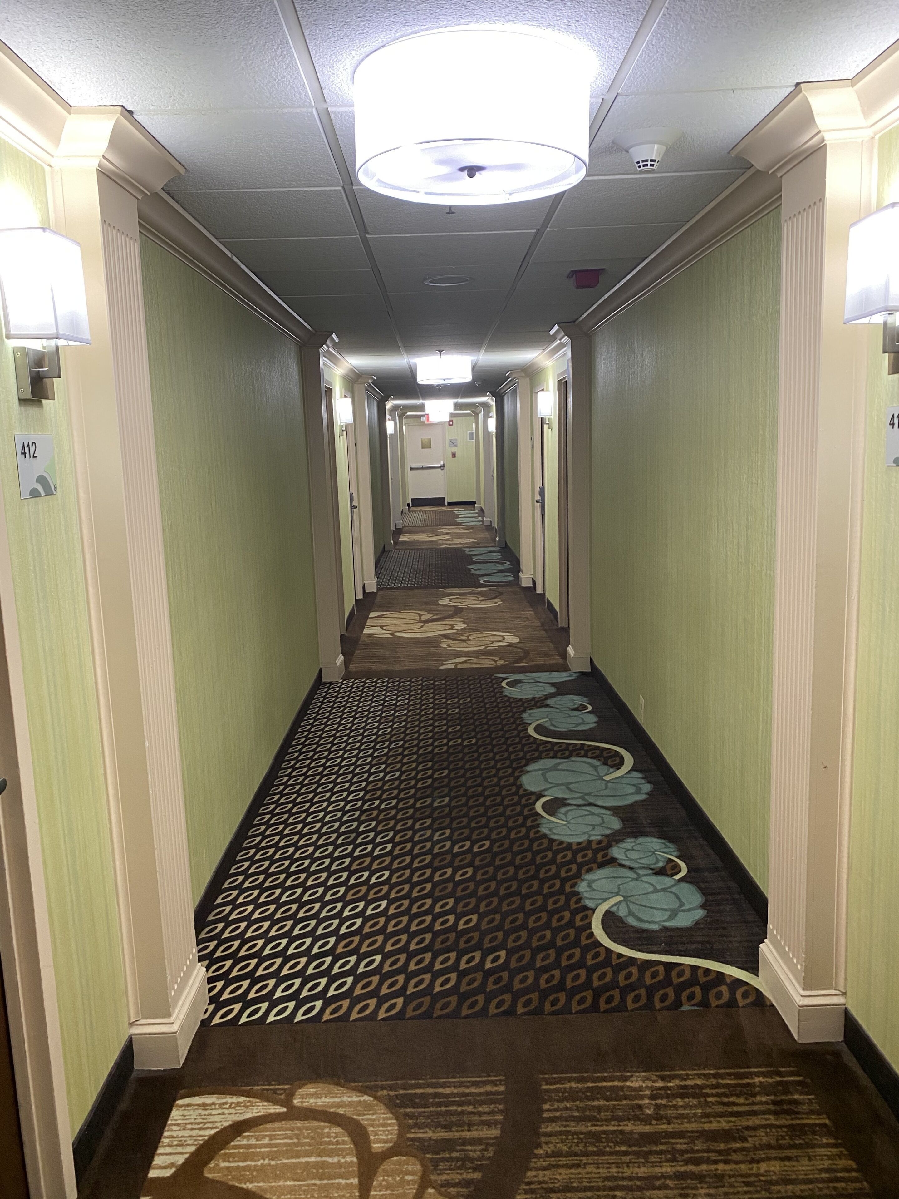 Un couloir d’hôtel avec un tapis à motifs, des murs verts et des portes numérotées 412 et 413.