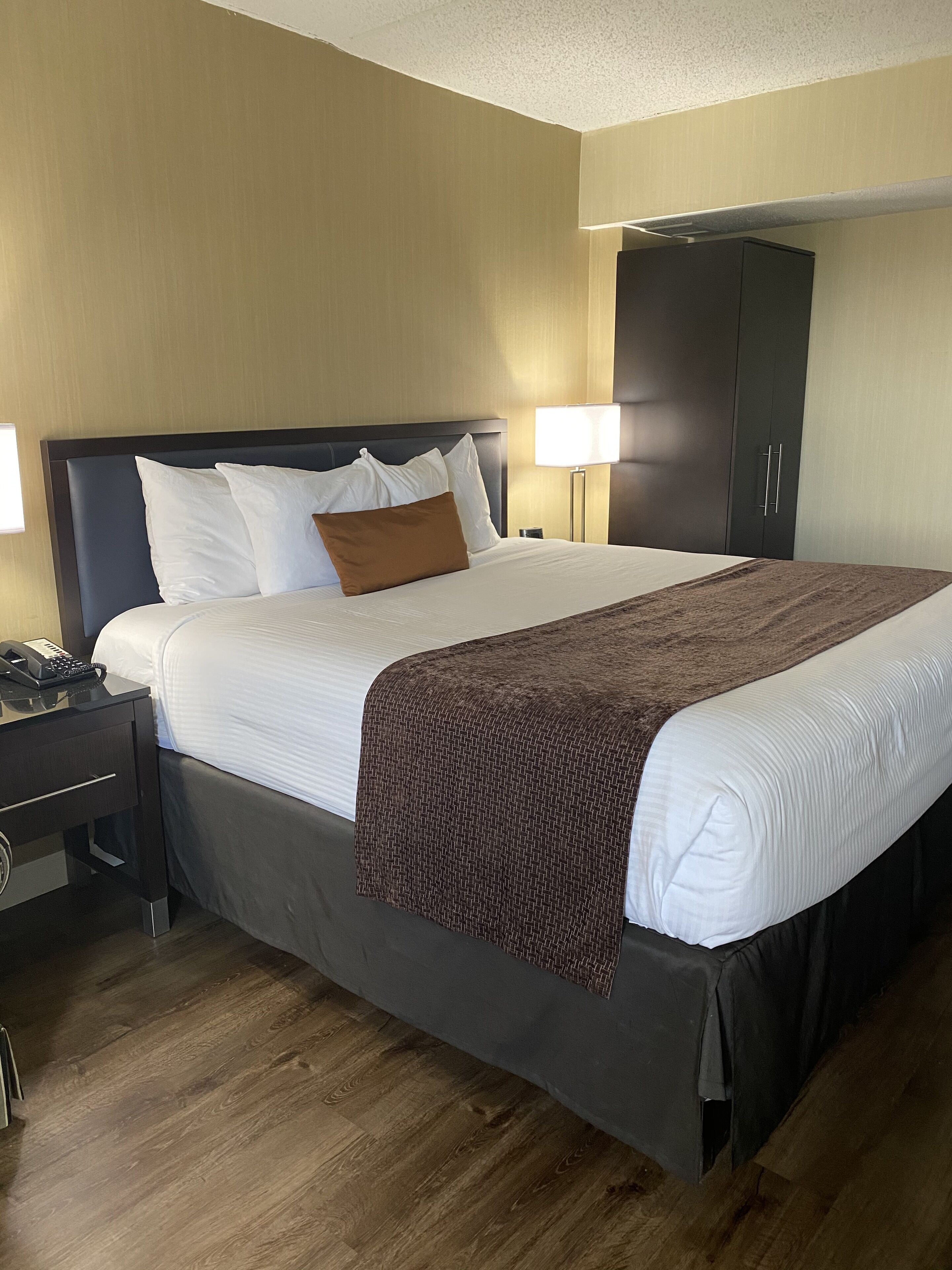 Una habitación de hotel con una cama grande, una mesita de noche con un teléfono, una lámpara y un armario.