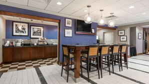 A hotel lobby with a checkered floor, a bar area with a counter and chairs, and framed pictures on the walls.