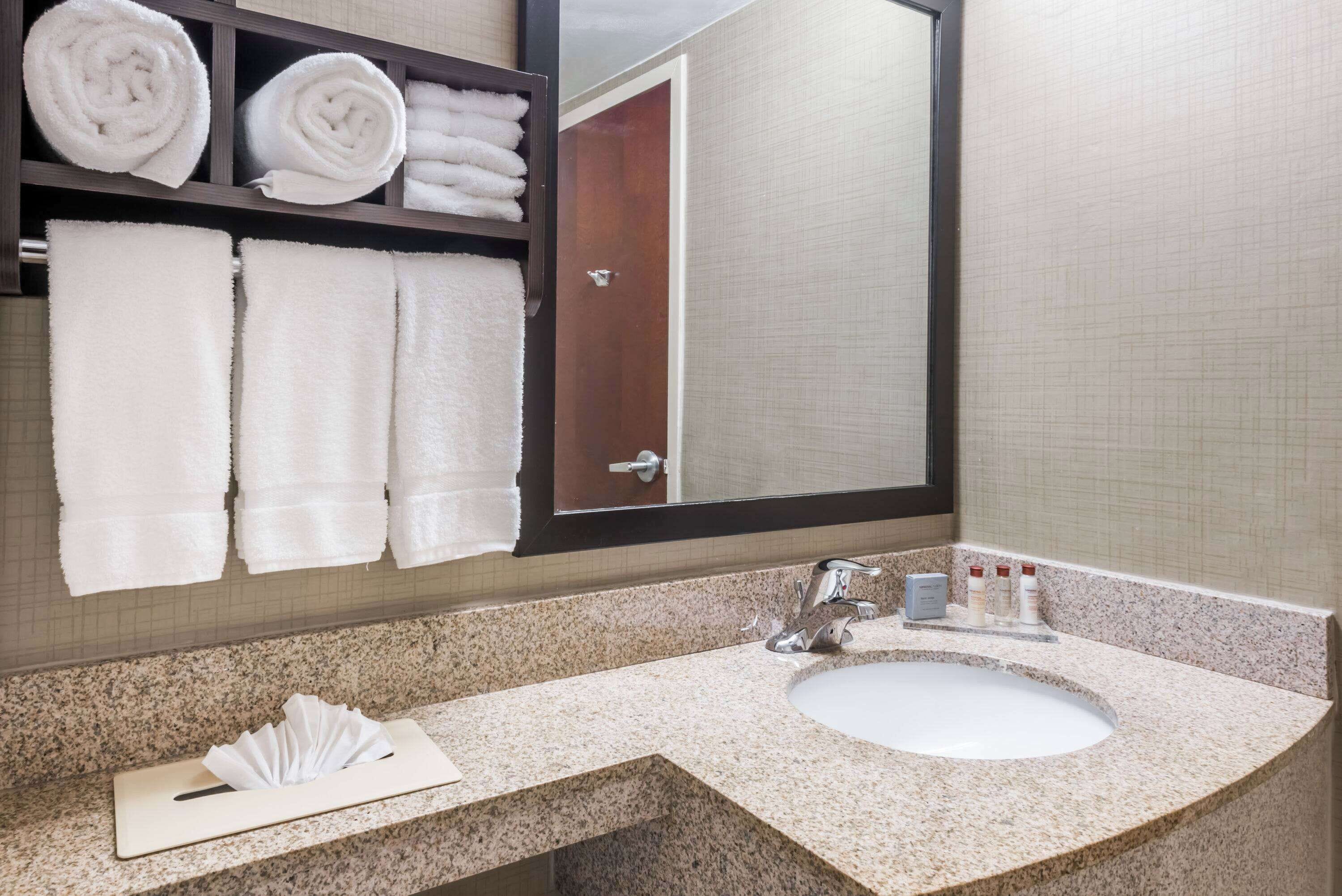 A bathroom with a granite countertop, a white sink, and a towel rack with neatly folded towels.