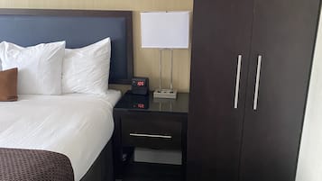 Une chambre d’hôtel comprenant un lit, une table de chevet avec une horloge, une lampe et une armoire.