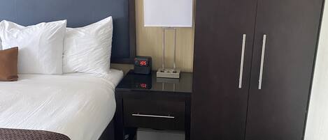 Une chambre d’hôtel comprenant un lit, une table de chevet avec une horloge, une lampe et une armoire.