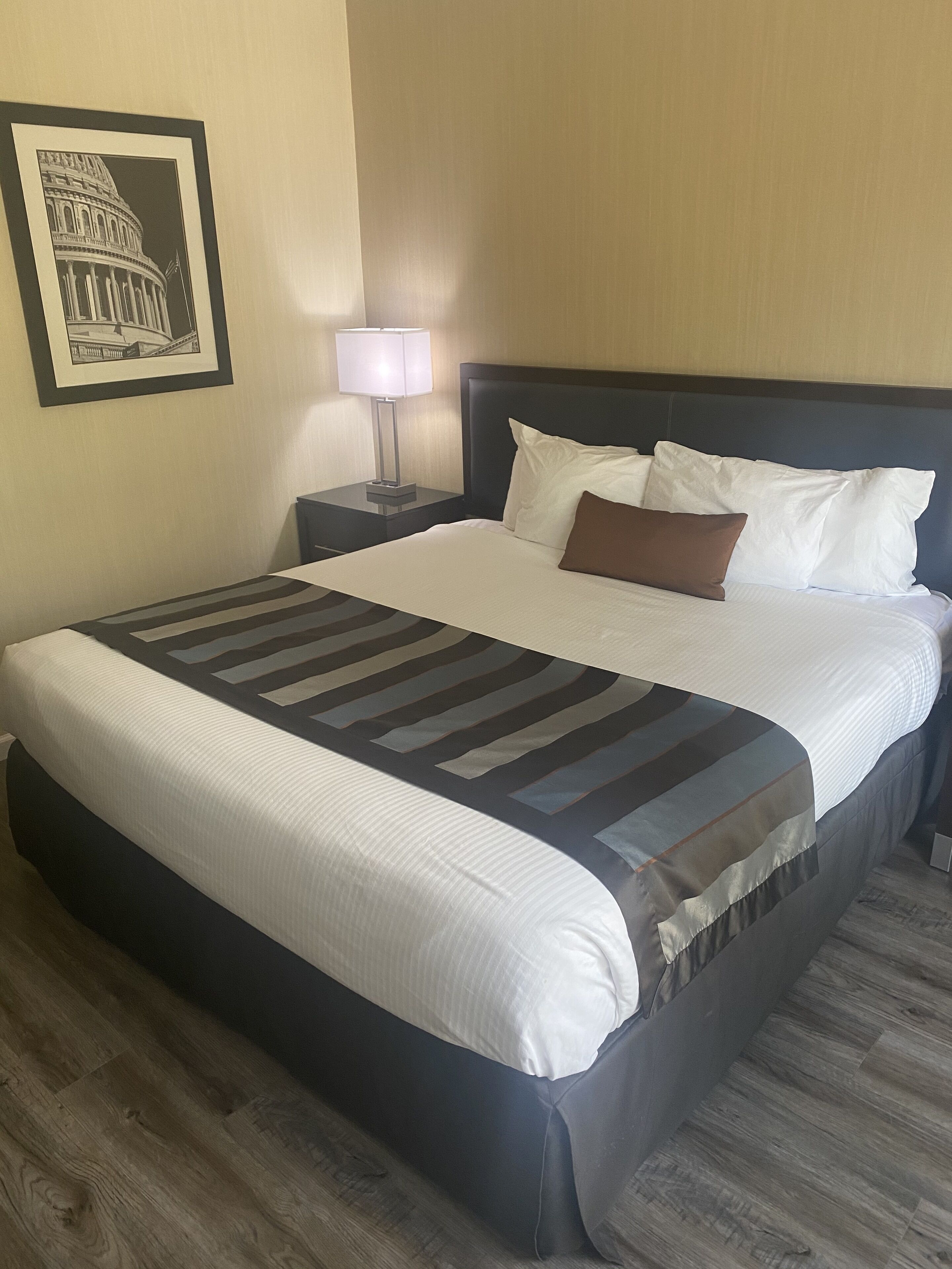 A hotel room with a large bed, a nightstand with a lamp, and a framed picture of a building on the wall.