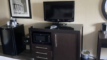 A hotel room with a bed, a television, a microwave, a small refrigerator, a trash can, and a framed picture of the Capitol building.