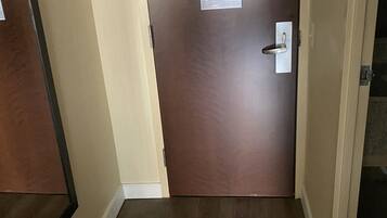 Un pasillo con piso de madera, paredes beige y una puerta marrón con un papel pegado.