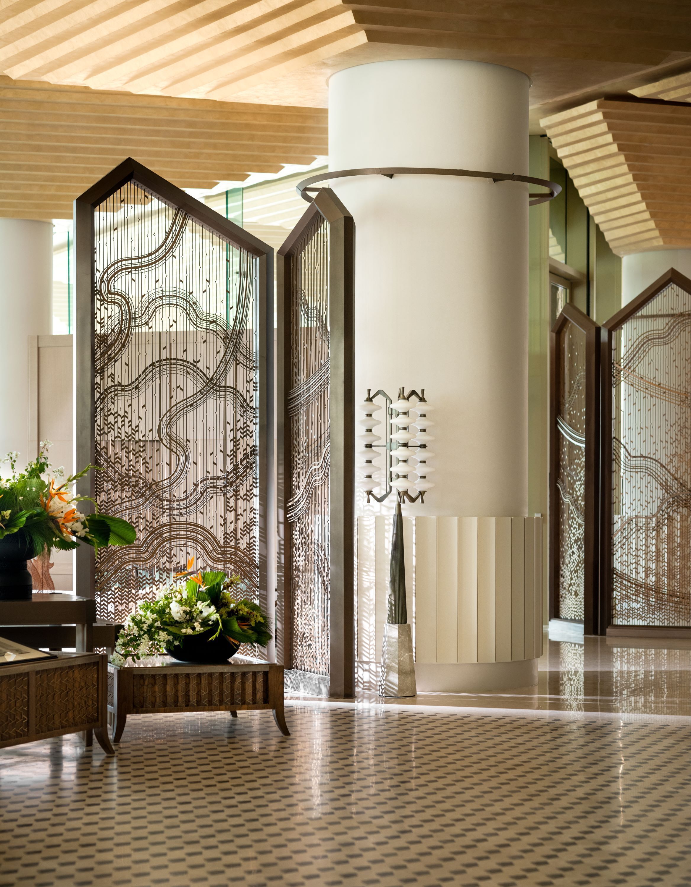 A modern lobby with a patterned partition, a tall cylindrical column, and a floor with a diamond pattern.