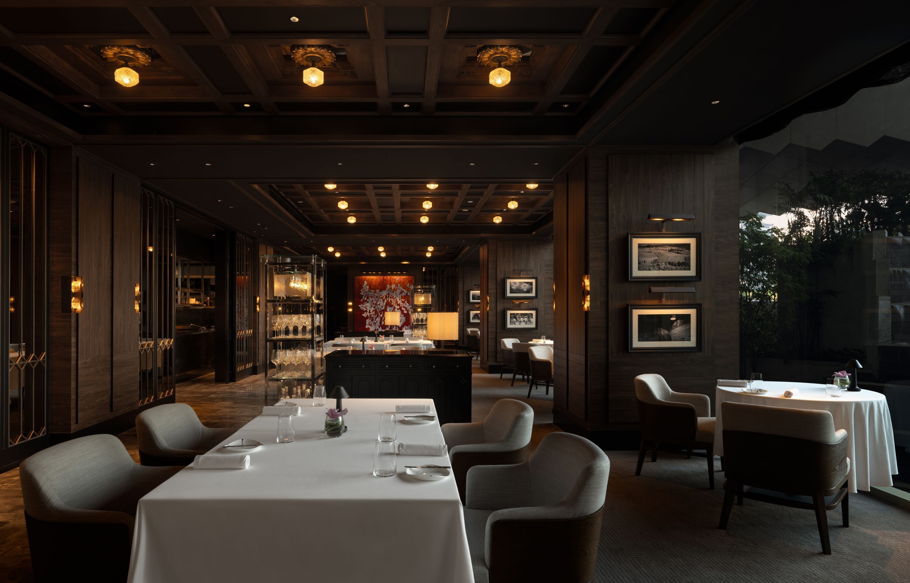 A restaurant with a long counter, multiple tables, and chairs. There are framed pictures on the walls and a bar area in the background.