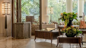 A modern lobby with a geometric patterned wall, a reception desk, seating area, and a large window with a view of greenery.
