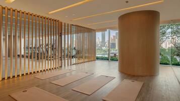 A spacious room with wooden flooring, large windows offering a city view, and exercise mats arranged for use.