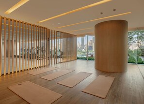 A spacious room with wooden flooring, large windows offering a city view, and exercise mats arranged for use.
