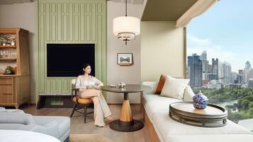 A modern hotel room with a city view, a green accent wall, a round table, and a sofa with a decorative bowl.