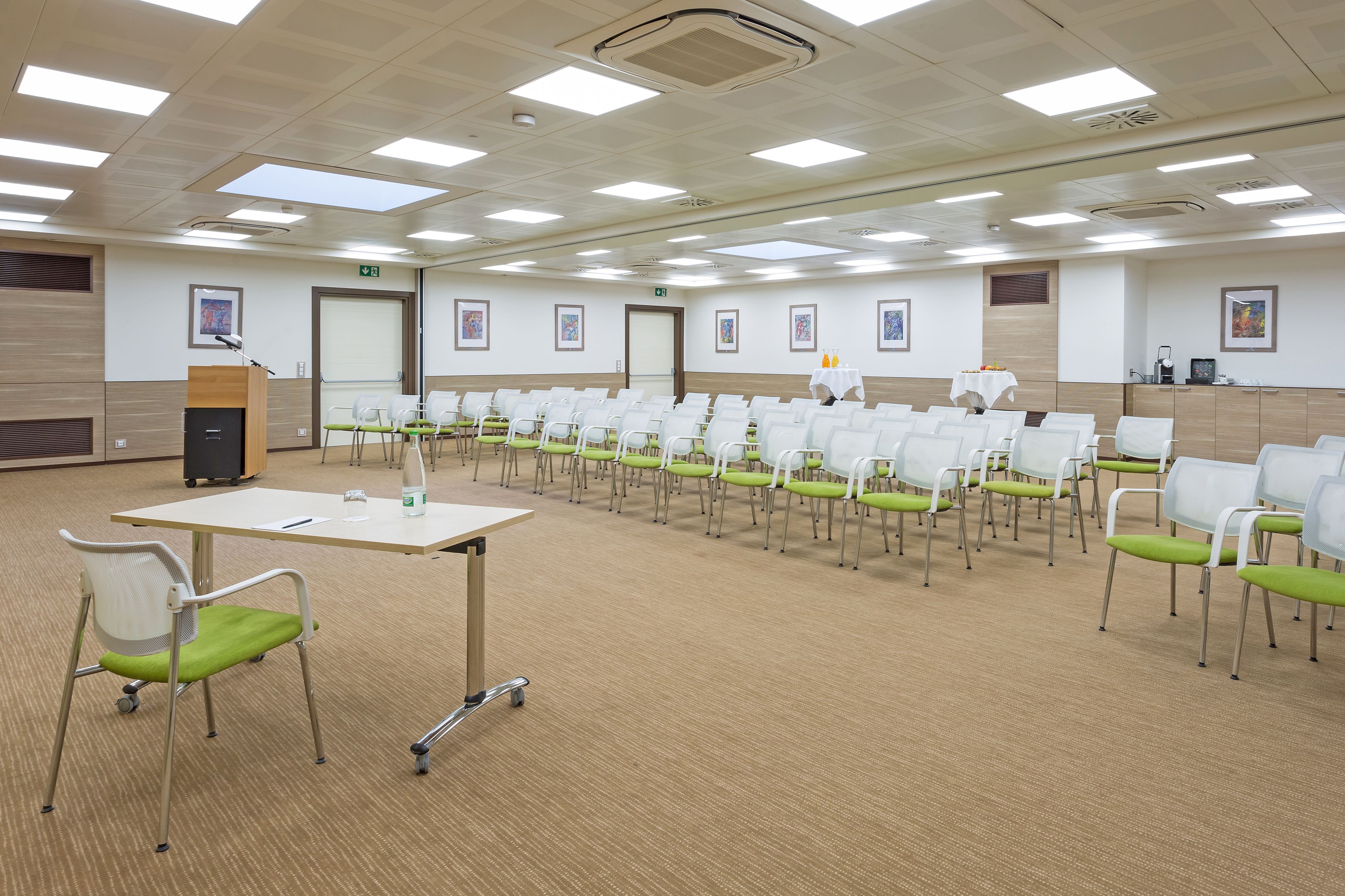 Un salón de conferencias con filas de sillas blancas, un atril y suelo alfombrado.