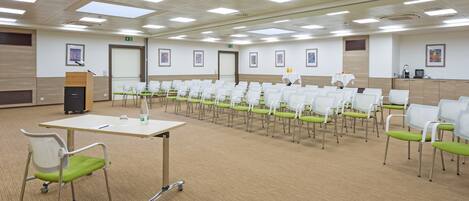 A conference room with rows of white chairs, a podium, and a carpeted floor.