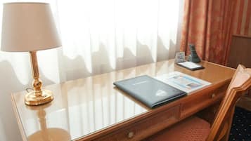 A hotel room with a glass desk, a lamp, a phone, a brochure, and a chair.
