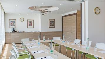 Une salle de conférence avec de longues tables, des chaises et des bouteilles d’eau.