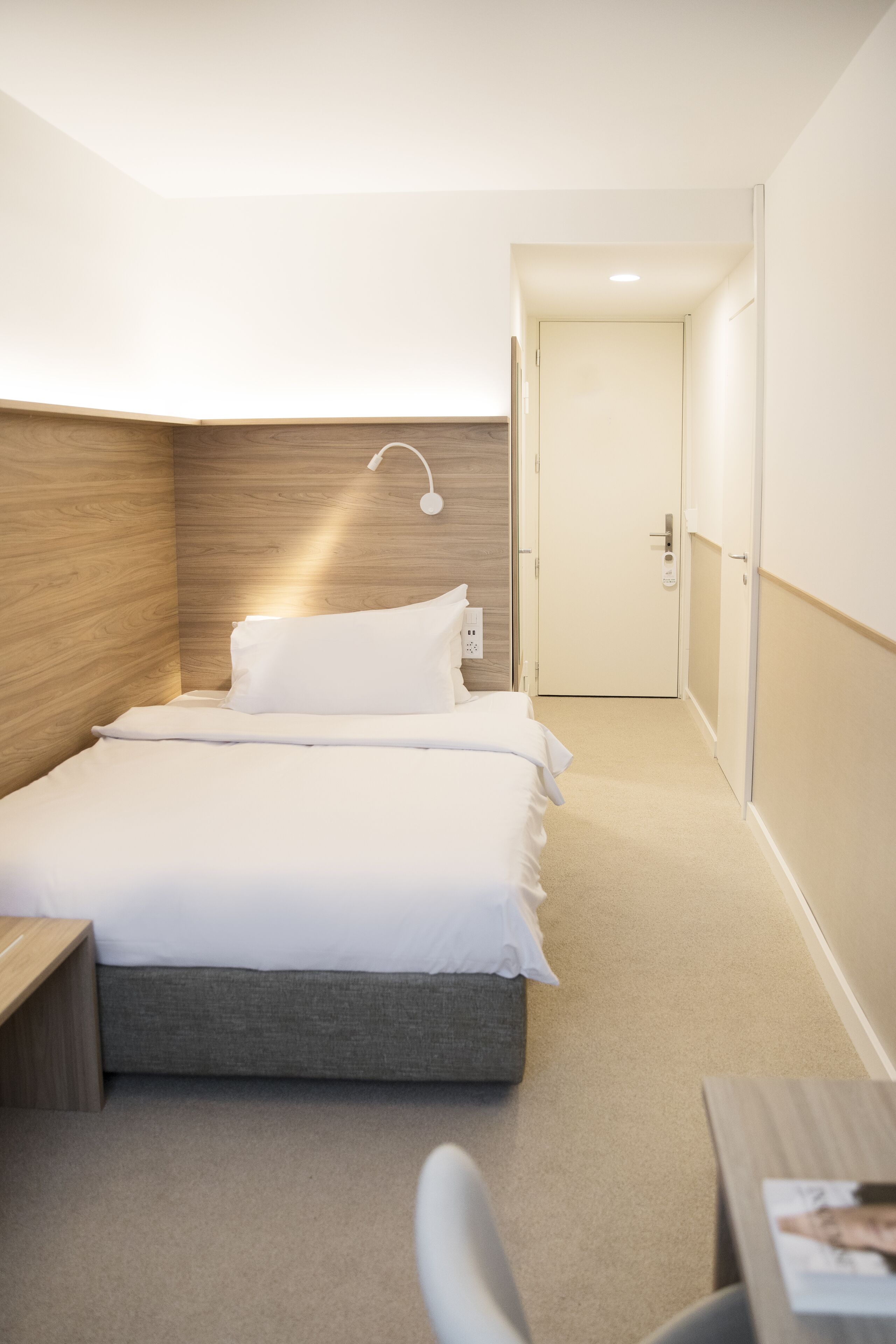 Quarto de hotel com cama, mesa de cabeceira e escrivaninha com cadeira.