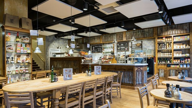 Un café acogedor con mesas y sillas de madera, una zona de bar y estantes llenos de bocadillos y bebidas.