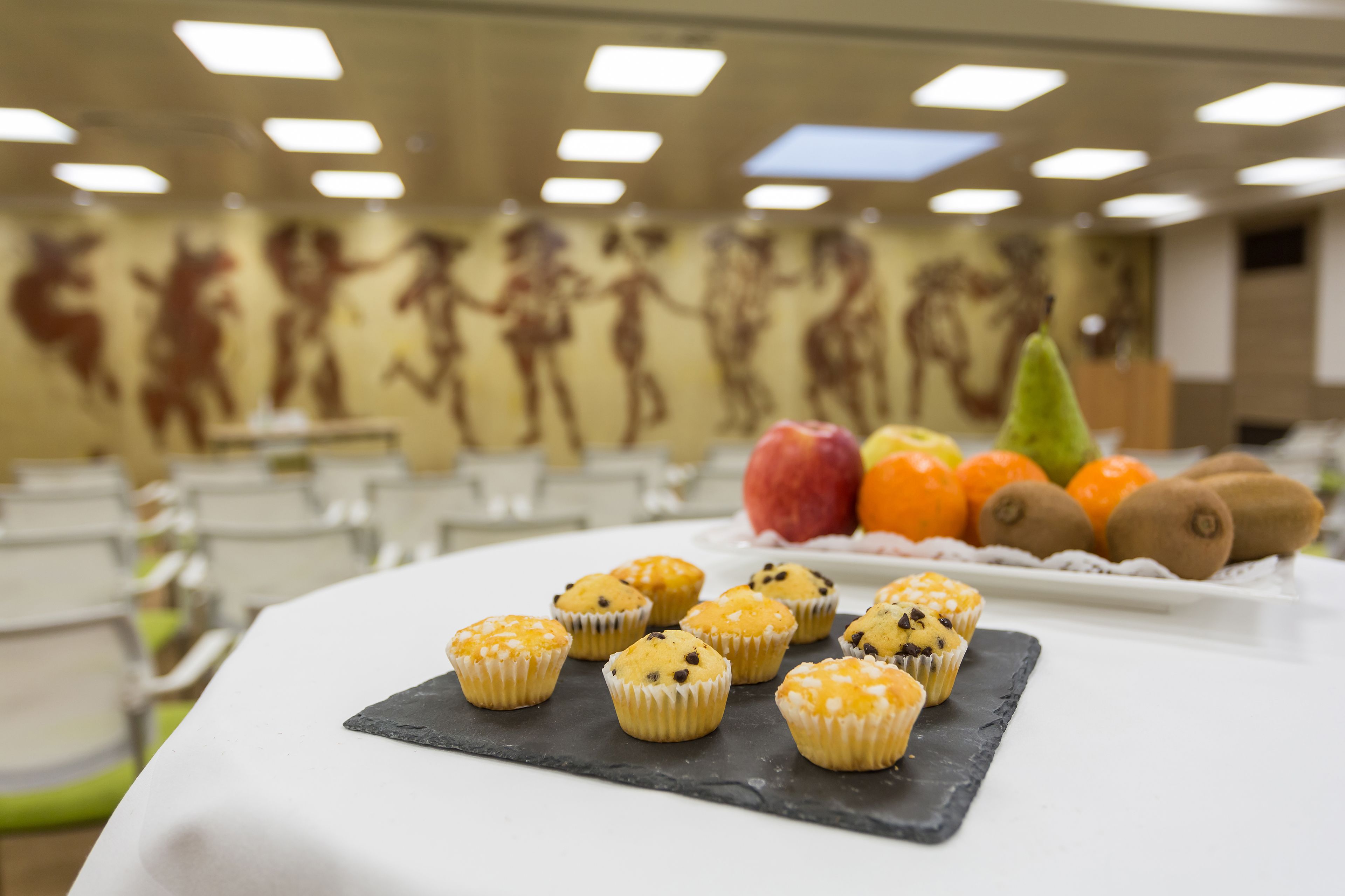 Una mesa con muffins y frutas en una habitación con un mural en la pared.