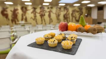 A table with muffins and fruits in a room with a mural on the wall.