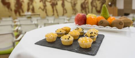 Una mesa con muffins y frutas en una habitación con un mural en la pared.