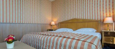 A hotel room with a bed, two bedside tables, a nightstand, a lamp, and a vase with flowers.