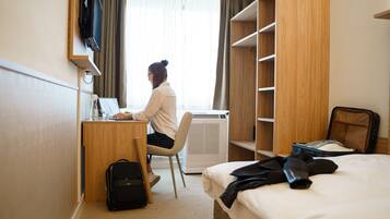 Ein Hotelzimmer mit Schreibtisch, Stuhl, Bett, Kleiderschrank und Koffer.