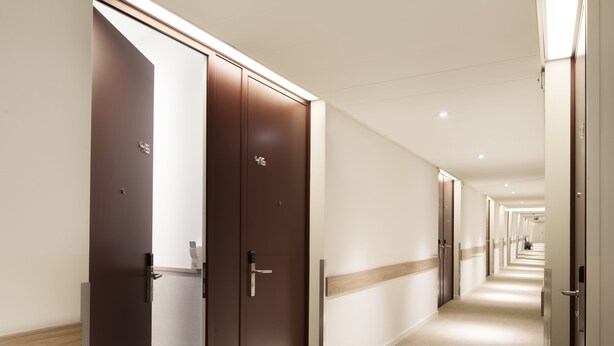 A hotel corridor with multiple doors, carpeted floors, and recessed lighting. - Hotel Continental (Lausanne)