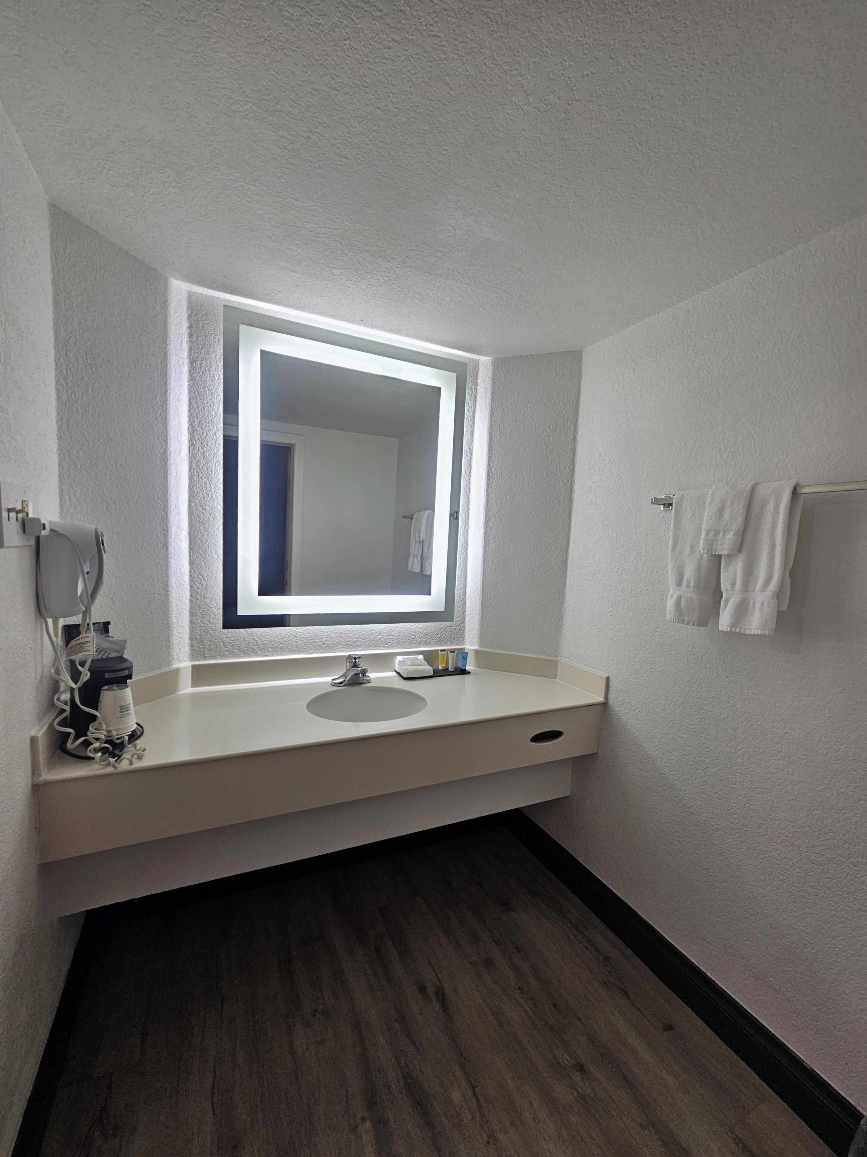 Un baño con lavamanos blanco, un espejo y un perchero para toallas.