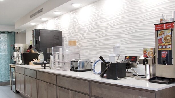 A modern hotel reception area with a coffee machine, a toaster, and a vending machine. - Ramada by Wyndham Westminster Denver (Westminster)