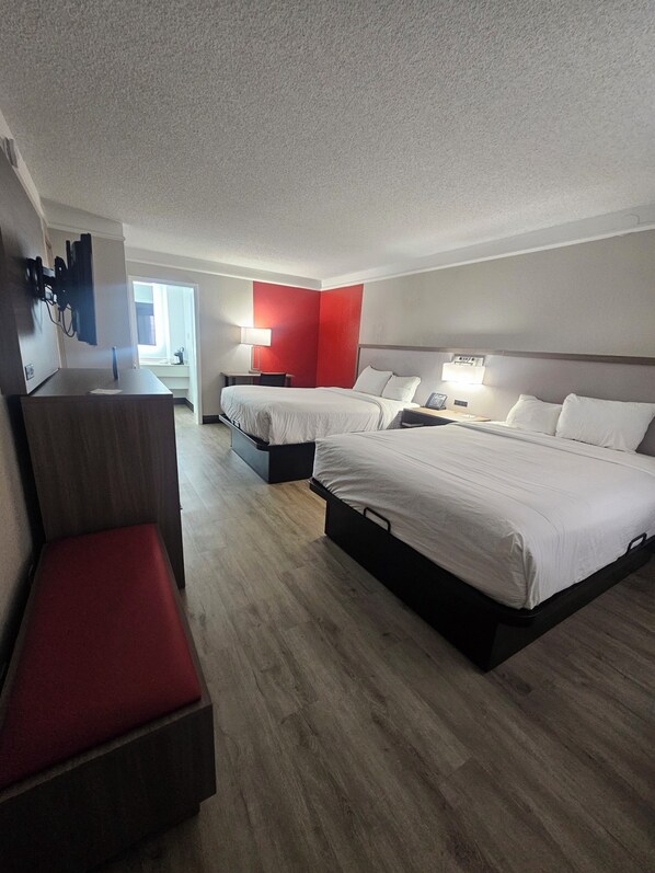 A hotel room with two beds, a desk, a chair, and a red accent wall.